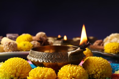 Diwali celebration. Diya lamp, colorful rangoli and chrysanthemum flowers on table against violet background, closeup