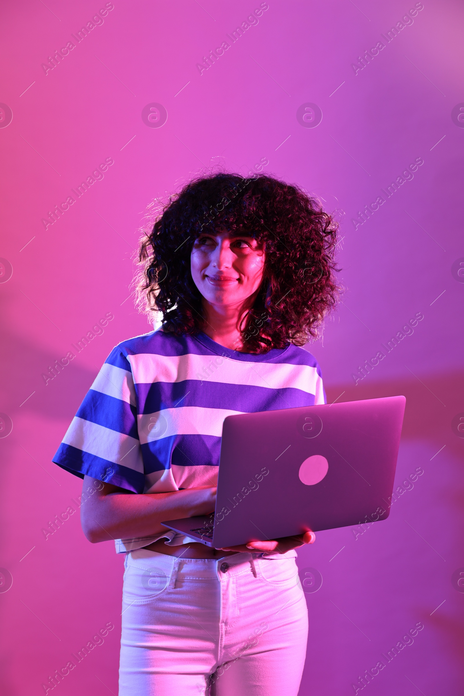 Photo of Beautiful young woman with laptop on color background in neon lights