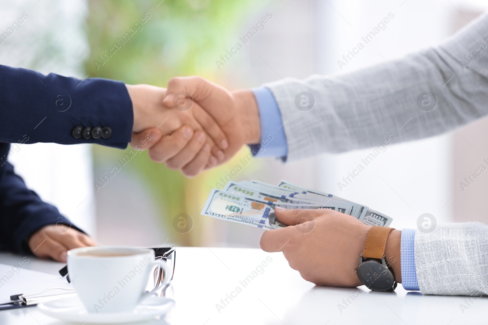 Photo of Man shaking hands with woman and offering bribe at table in office