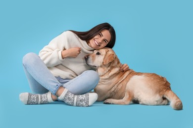 Happy woman playing with cute Labrador Retriever on light blue background