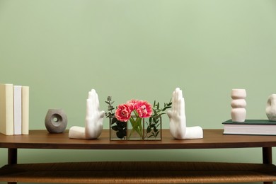 Photo of Wooden coffee table with flowers and decor elements near pale green wall indoors. Stylish interior design