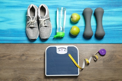 Photo of Flat lay composition with scales, apples and sport equipment on wooden background. Weight loss