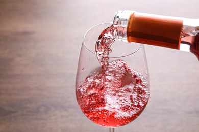 Pouring delicious rose wine into glass on wooden table, closeup