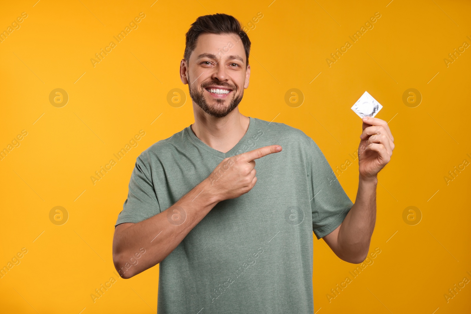 Photo of Happy man holding condom on orange background