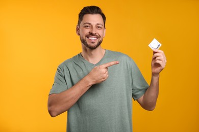 Happy man holding condom on orange background