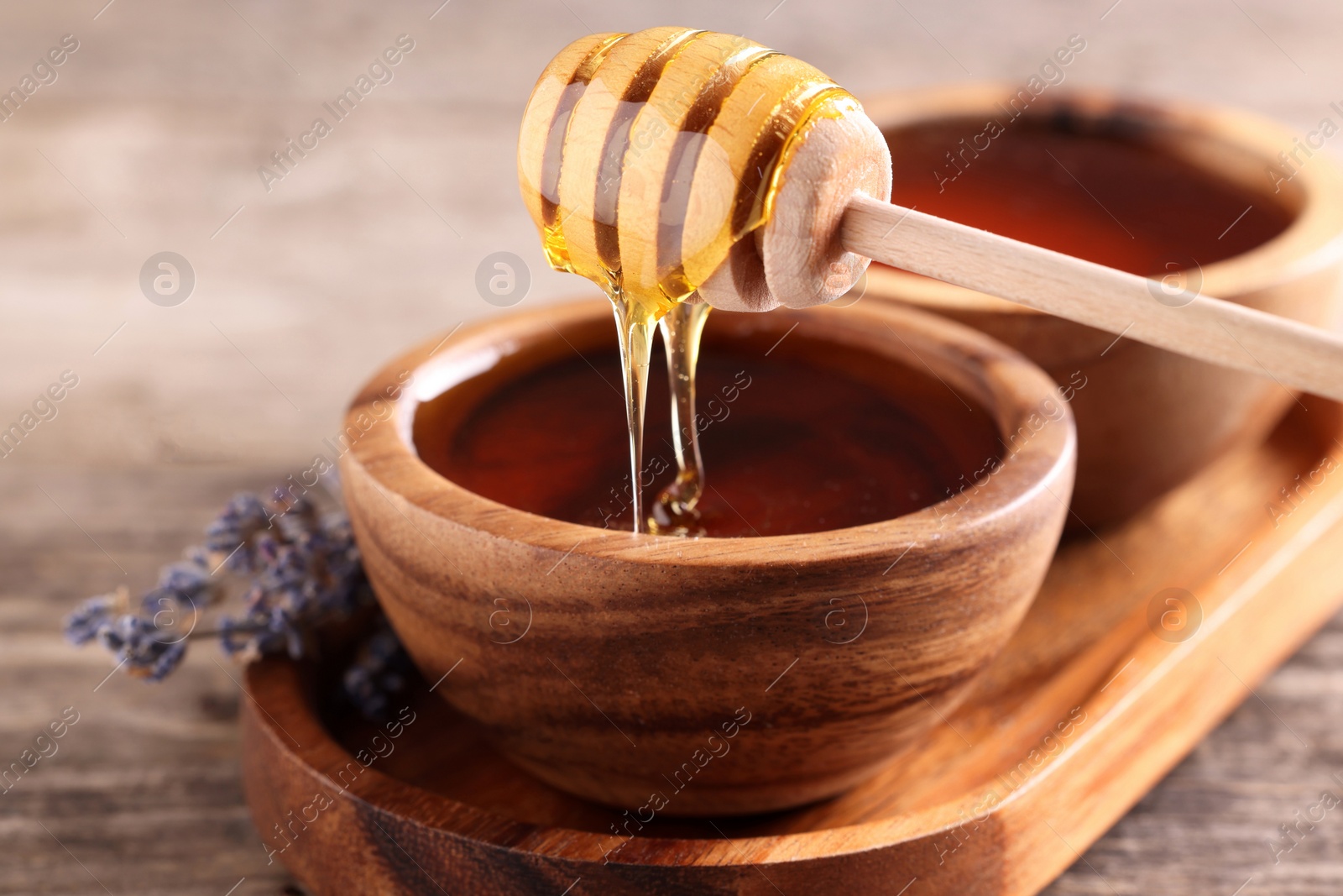 Photo of Pouring delicious honey from dipper into bowl on wooden table, closeup