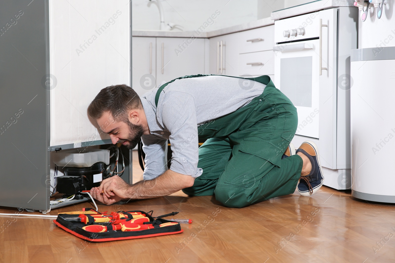 Photo of Male technician in uniform repairing refrigerator indoors