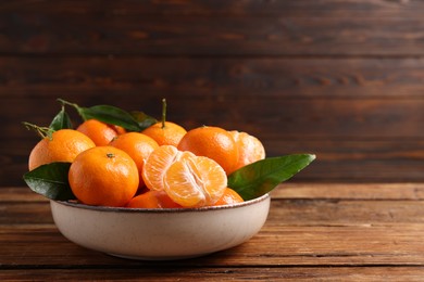 Fresh tangerines with green leaves in bowl on wooden table, space for text