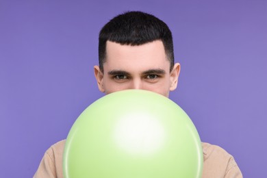 Young man inflating light green balloon on purple background