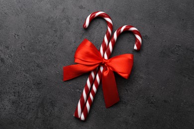 Photo of Sweet Christmas candy canes with red bow on grey background, top view