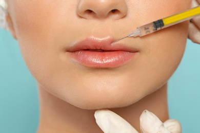 Young woman getting lips injection on color background, closeup. Cosmetic surgery