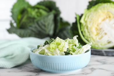 Chopped fresh green savoy cabbage in bowl on white marble table