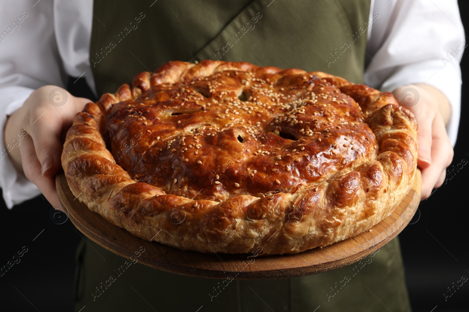 Photo of Woman holding tasty homemade pie on black background, closeup