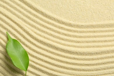 Photo of Zen rock garden. Wave pattern and green leaf on beige sand, top view