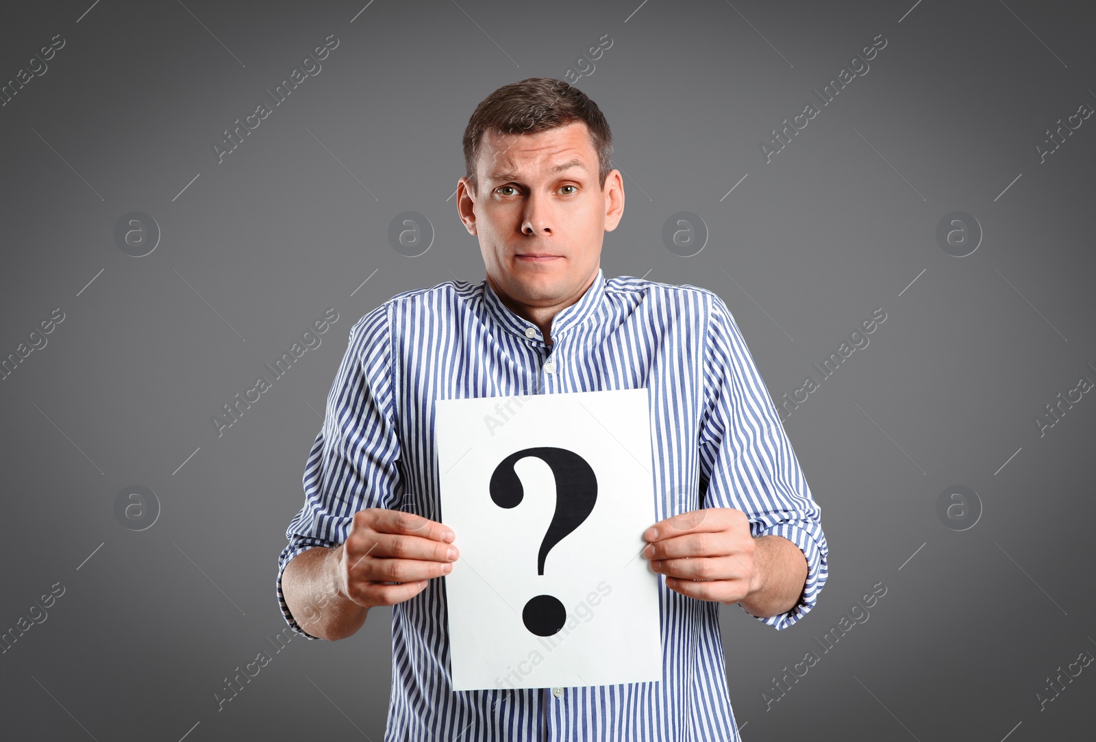 Photo of Emotional man holding paper with question mark on grey background