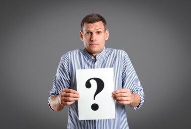 Photo of Emotional man holding paper with question mark on grey background