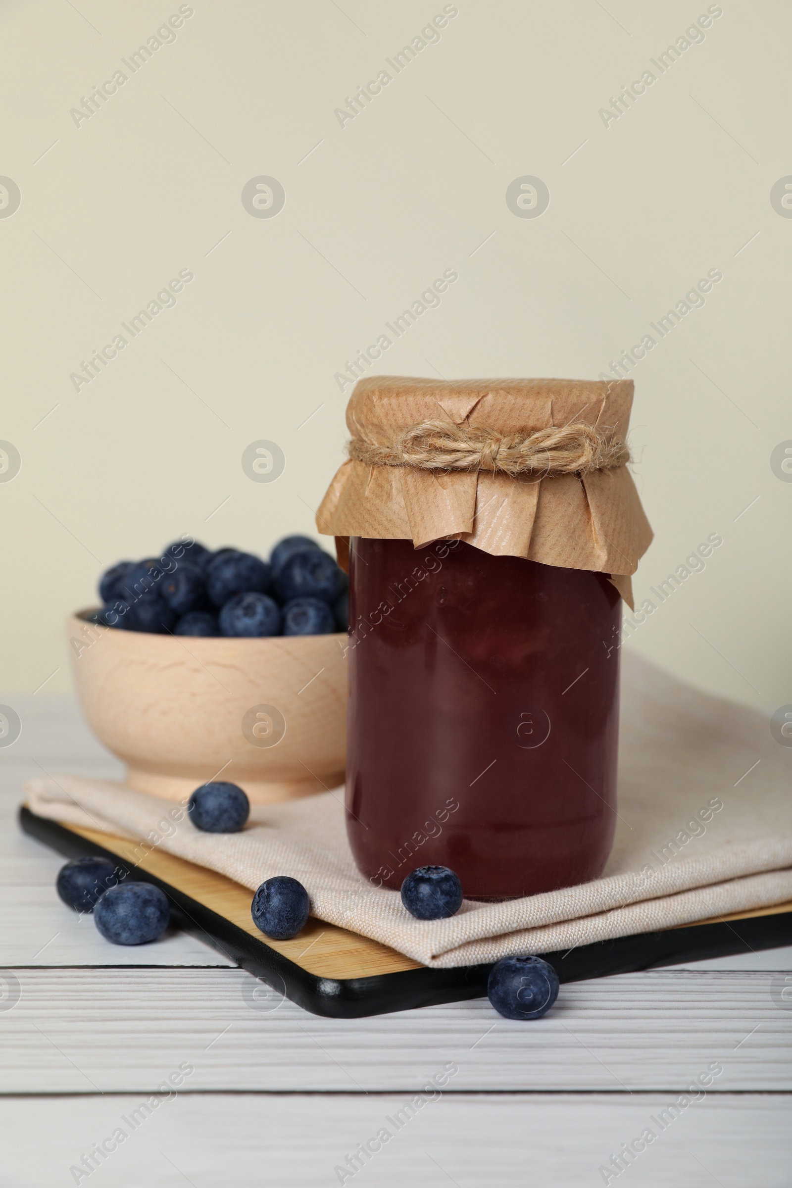 Photo of Jar of delicious blueberry jam and fresh berries on white wooden table