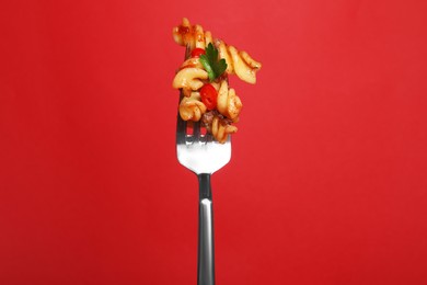Fork with tasty pasta on red background
