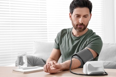 Man measuring blood pressure at wooden table in room, space for text