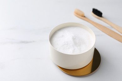 Photo of Bamboo toothbrushes and bowl of baking soda on white marble table, closeup. Space for text