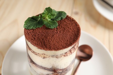 Photo of Tasty tiramisu and mint in glass on light table, closeup