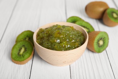 Photo of Bowl of delicious kiwi jam and fresh fruits on white wooden table