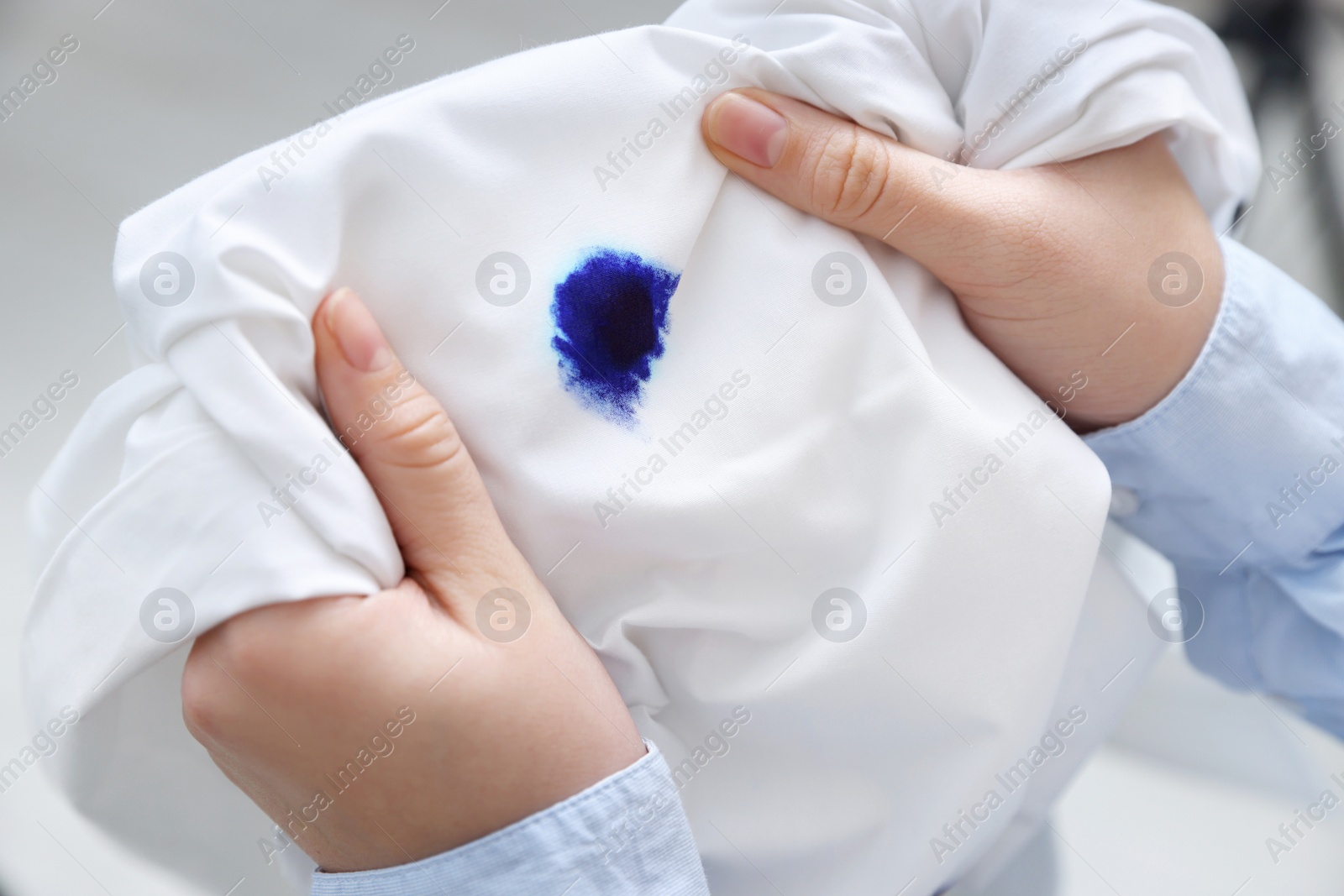 Photo of Woman holding white shirt with blue ink stain on blurred background, closeup