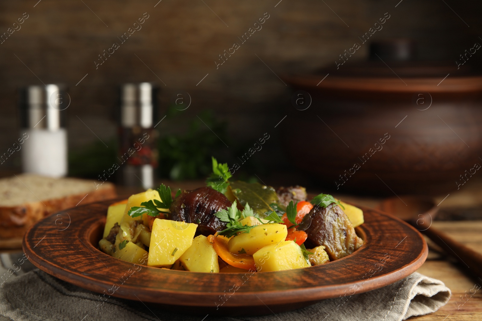 Photo of Tasty cooked dish with potatoes in earthenware on wooden table