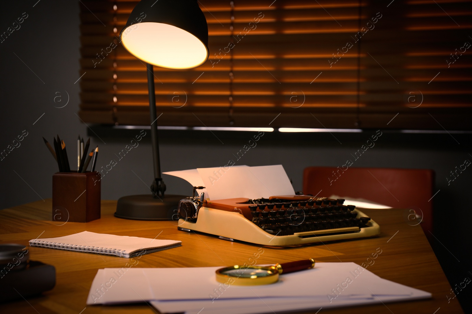Photo of Typewriter, magnifying glass and papers on desk in office. Detective's workplace