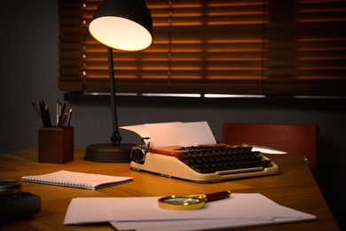 Typewriter, magnifying glass and papers on desk in office. Detective's workplace