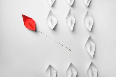 Photo of Red paper boat floating away from others on white background, flat lay. Uniqueness concept