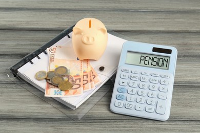 Photo of Calculator, piggy bank, euro banknotes, coins and folder on wooden table. Pension planning