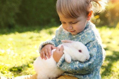 Photo of Cute little girl with adorable rabbit outdoors on sunny day. Space for text