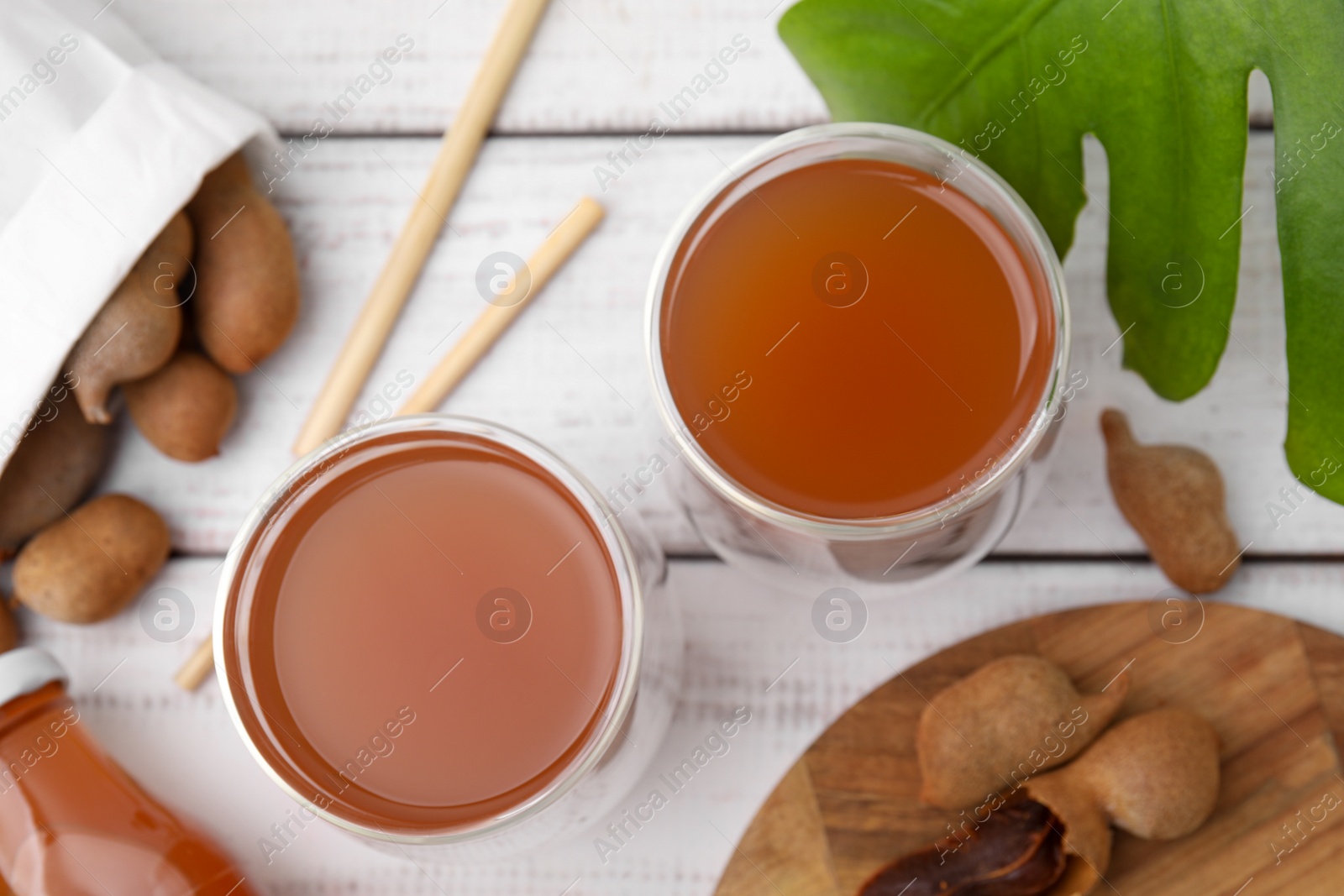 Photo of Tamarind juice and fresh fruits on white wooden table, flat lay