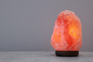 Himalayan salt lamp on stone table near light grey wall, space for text