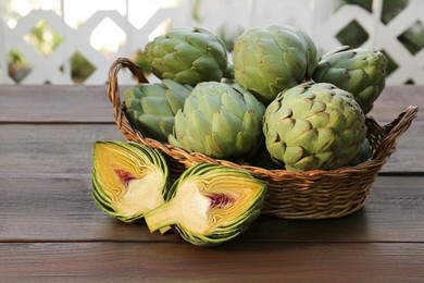 Wicker basket with fresh raw artichokes on wooden table