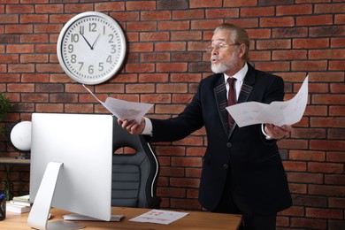 Photo of Angry senior boss holding paper sheets in modern office