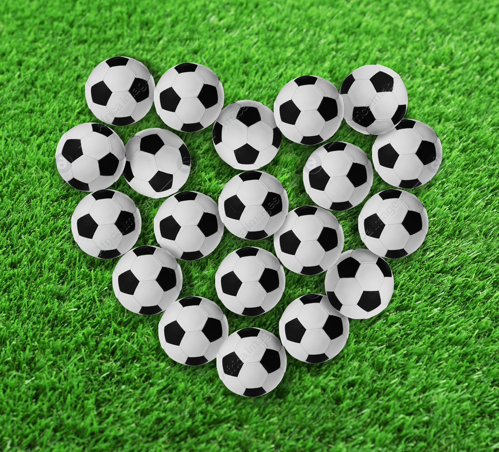 Image of Heart made of many soccer balls on green grass, top view