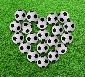 Image of Heart made of many soccer balls on green grass, top view