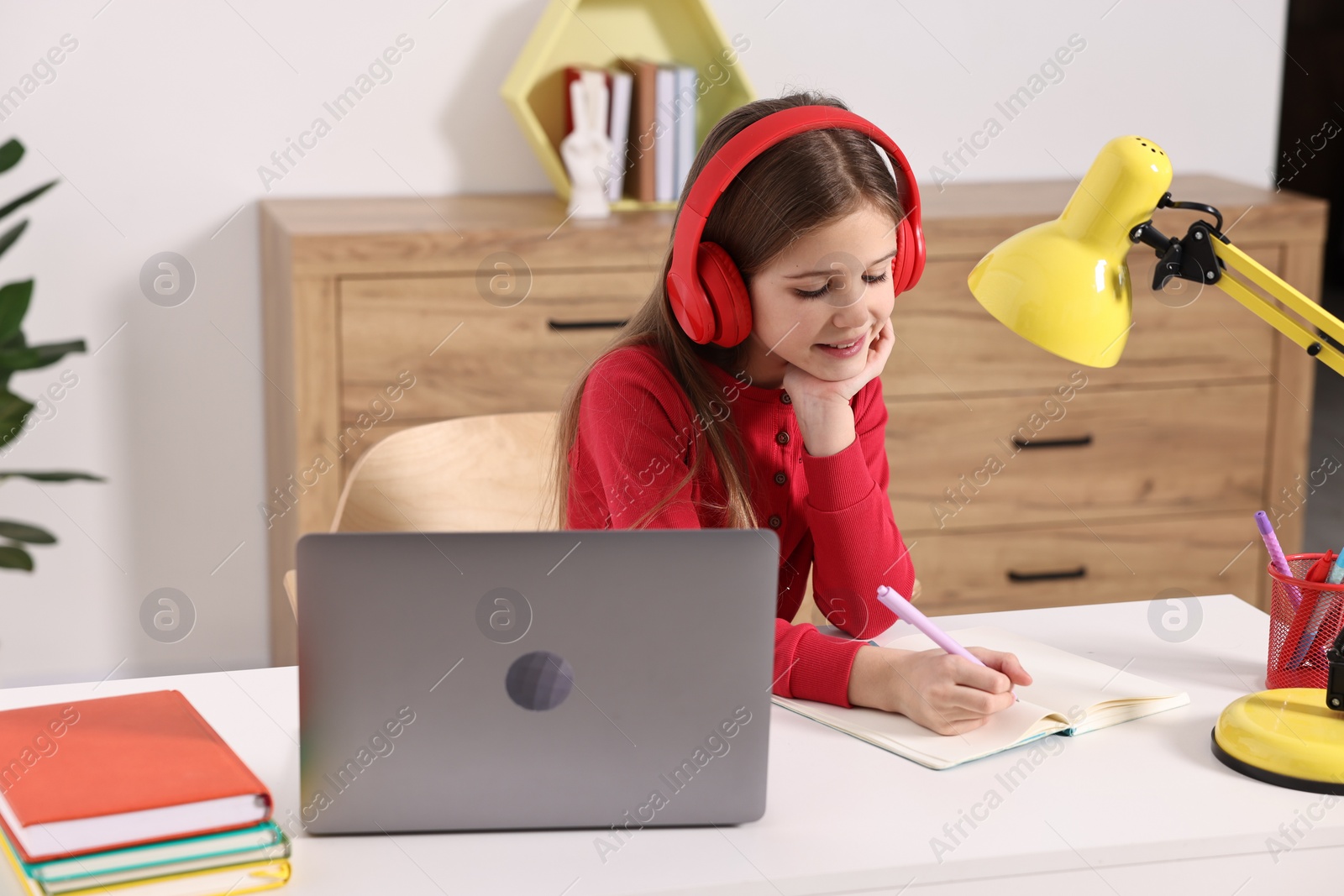 Photo of E-learning. Cute girl taking notes during online lesson at table indoors