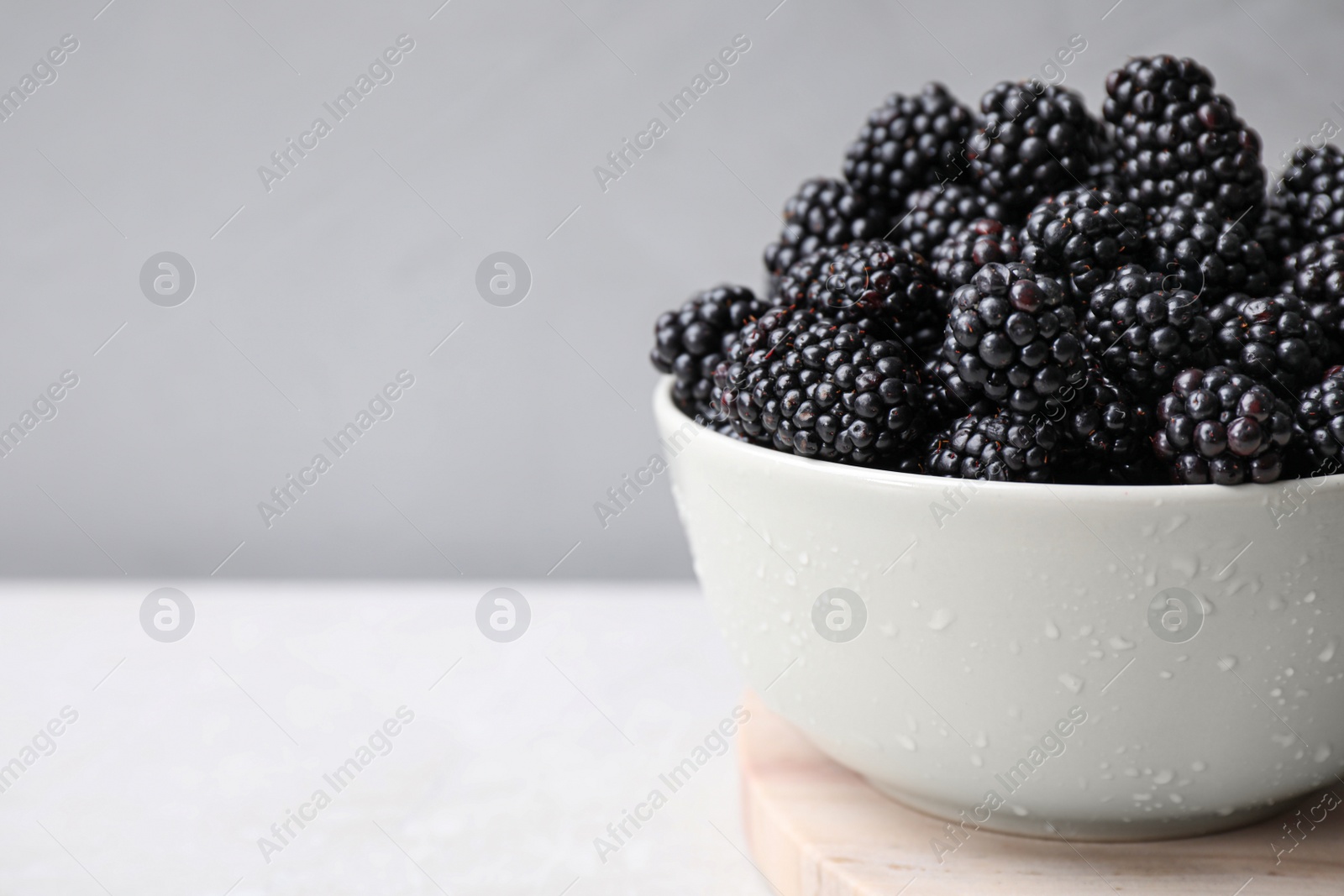 Photo of Fresh ripe blackberries in bowl on white table against grey background. Space for text