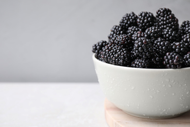 Fresh ripe blackberries in bowl on white table against grey background. Space for text