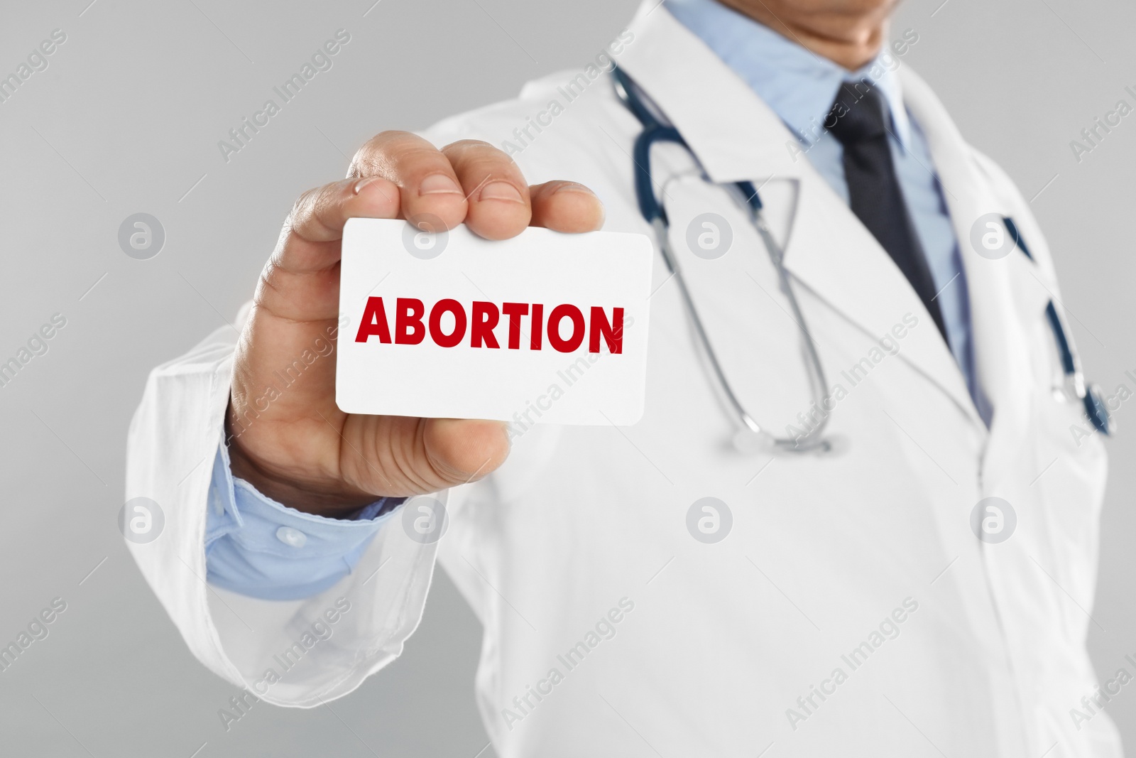 Image of Doctor holding paper card with word Abortion on light grey background, closeup