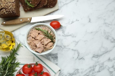 Bowl with canned tuna and products on white marble table, flat lay. Space for text