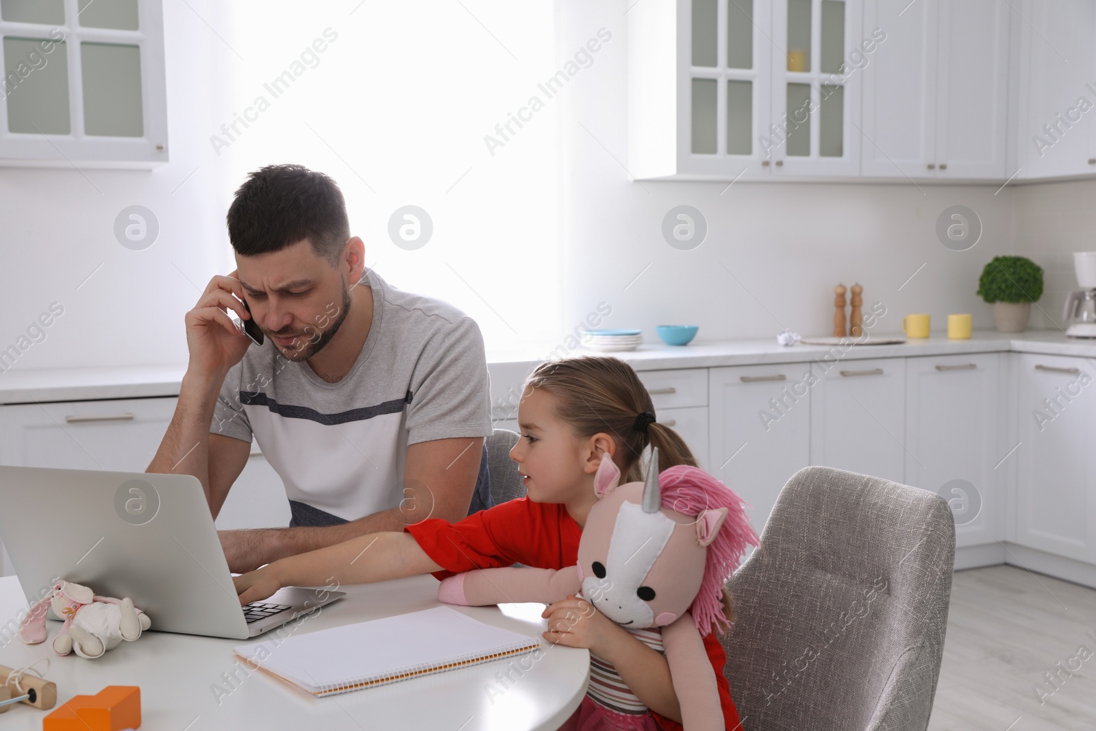 Photo of Cute child disturbing stressed man in kitchen. Working from home during quarantine