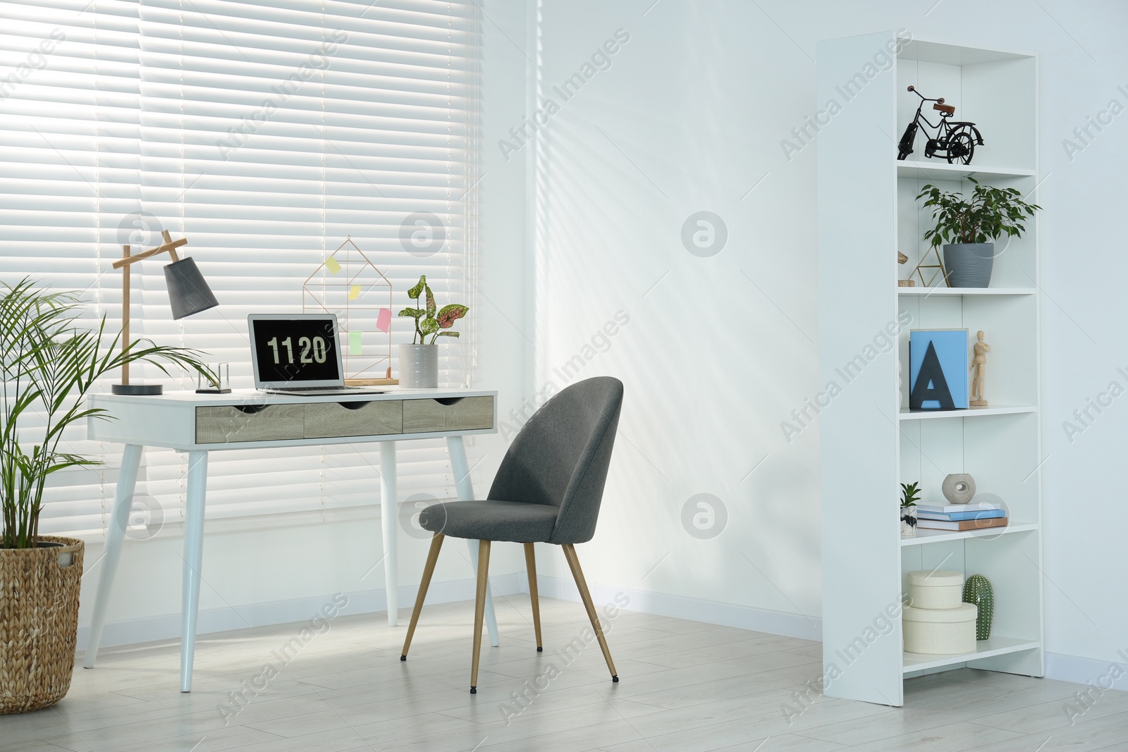 Photo of Cozy workspace with laptop, desk and comfortable chair at home. Stylish interior design