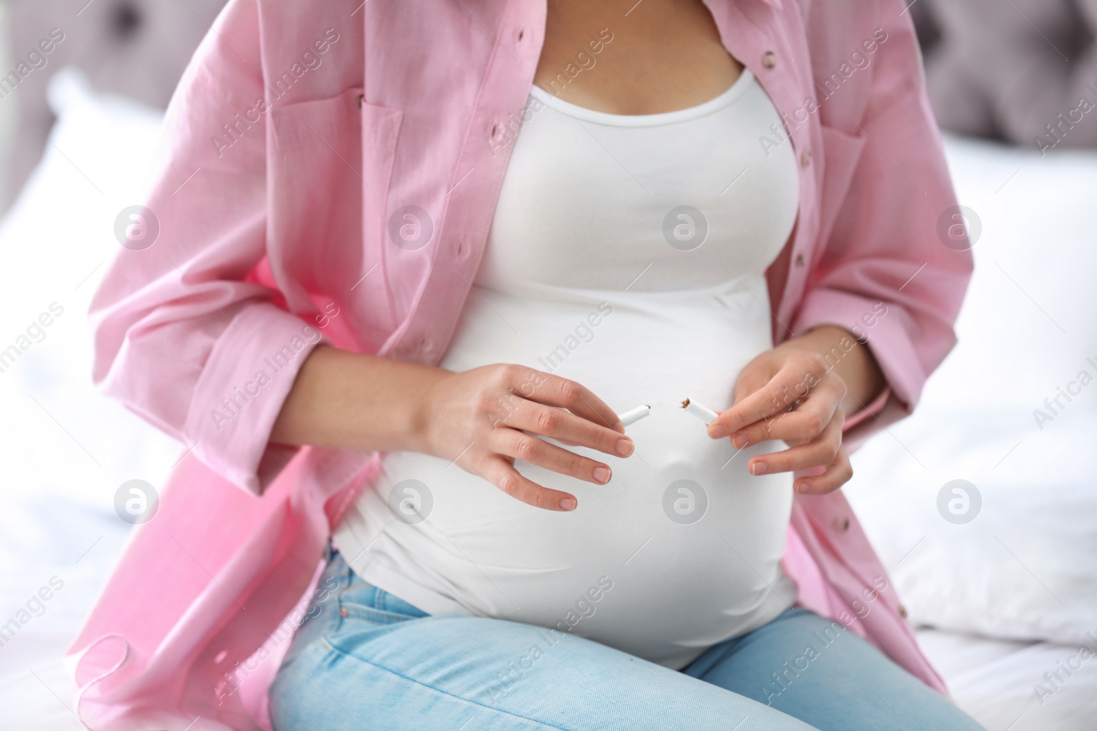 Photo of Young pregnant woman breaking cigarette in bedroom, closeup. Harm to unborn baby