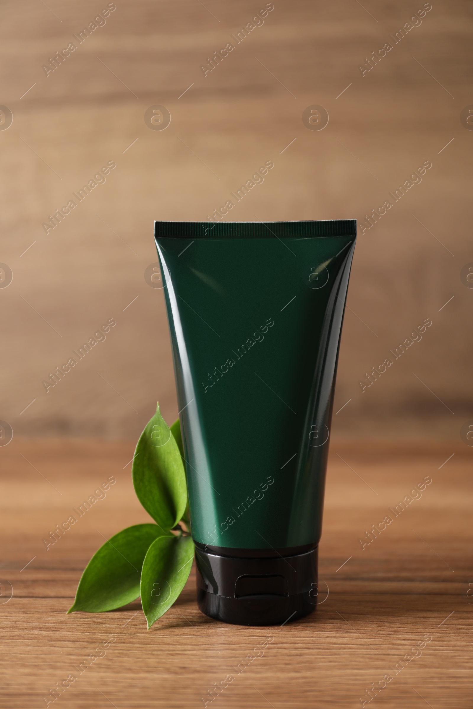 Photo of Tube of men's facial cream and green leaves on wooden table. Mockup for design