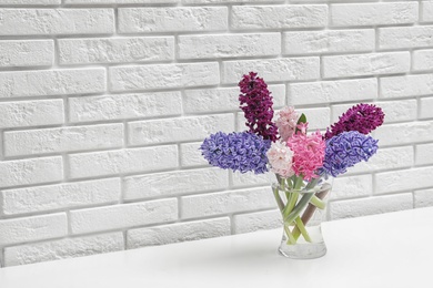 Photo of Beautiful hyacinths in glass vase on table against brick wall, space for text. Spring flowers