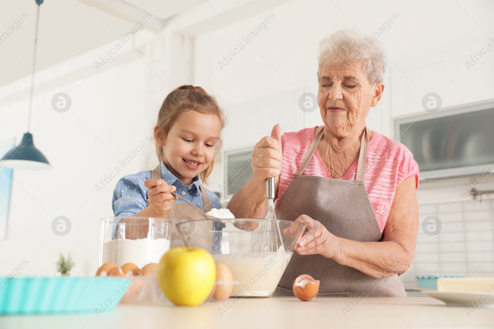 Photo of Cute girl and her grandmother cooking in kitchen